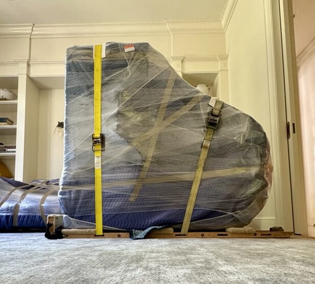 Movers handling a high-value item with protective padding